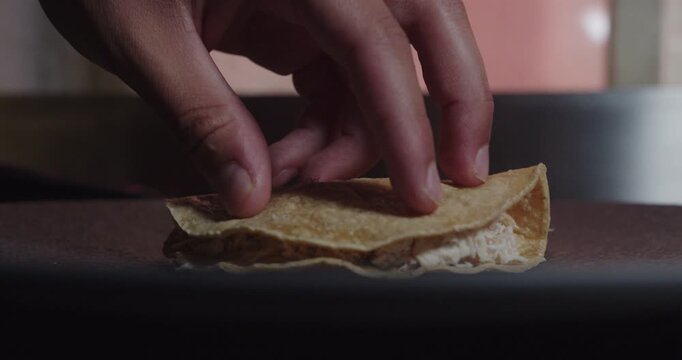 Beautiful slow motion close-up shot of a professional chef's hand folding a Mexican tortilla in half as a presentation for the dish of enchiladas in green sauce.