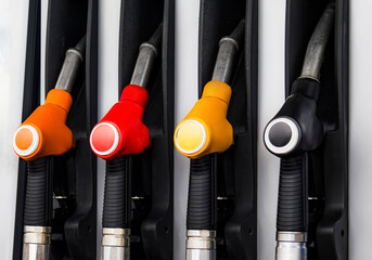 Four fuel dispensers with different colored nozzles are lined up at a gas station during daylight....