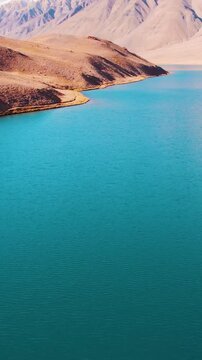 vertical aerial shot of Camera goes up and revealing beautiful view of Chandratal lake in Himalaya mountains at Spiti Valley, India. Blue water of mountain lake. Calm and Scenic beauty of nature. 