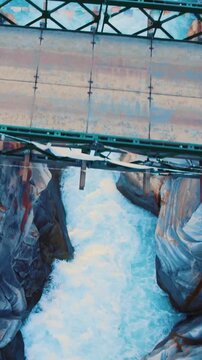 Vertical aerial shot of Bhaga river flowing between rocky canyon and wooden bridge passing above river stream. River in Lahaul, Himachal Pradesh, India. Old epic wooden bridge over blue river