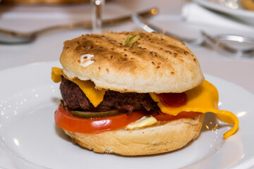 A popular American burger with minced beef, lettuce leaves, tomatoes, cheese, served in a soft bun. Freshly baked sandwich sprinkled with sesame seeds. delicious burger, burger menu, fast food.