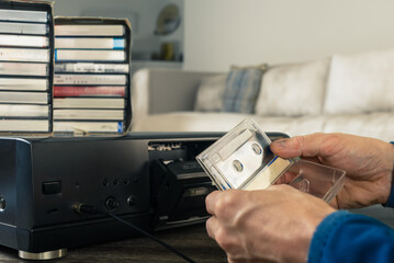Man in nostalgic mood changing cassette in old vintage tape recorder. Room echoes with nostalgia as...