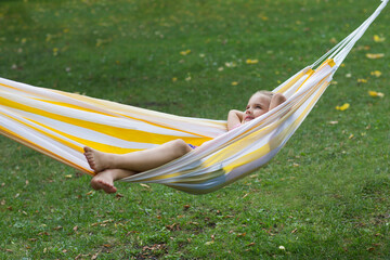 Happy  adorable smiling child girl in headphones listens to music lying in a hammock in summer park. Happy ghild having fun outdoors. Generation Alpha. copy space. favorite music.