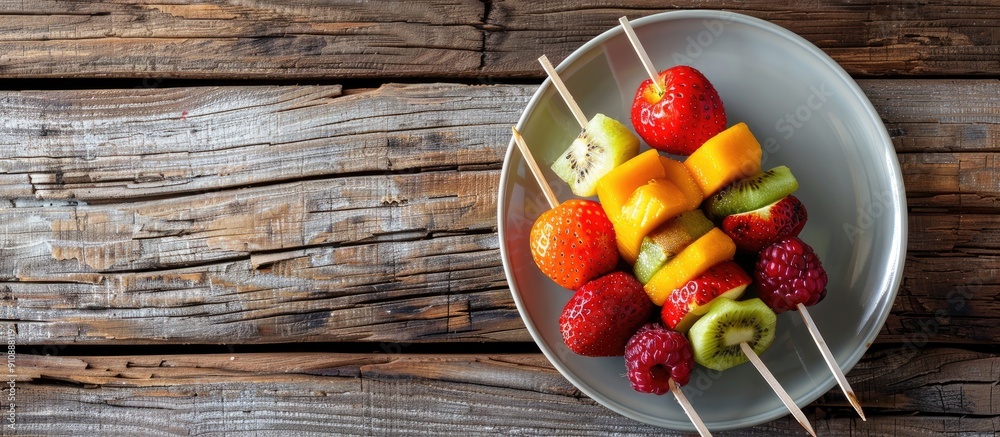 Poster Top view of a plate with skewered fresh fruits on a wooden table with ample copy space image