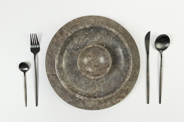 Top view of brown marble tray and plate, black cutlery on white background. Food presentation,...
