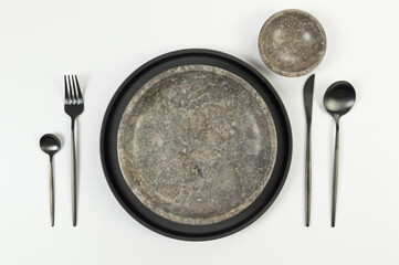 Top view of brown marble plate and bowl, black plate and cutlery on white background. Food...