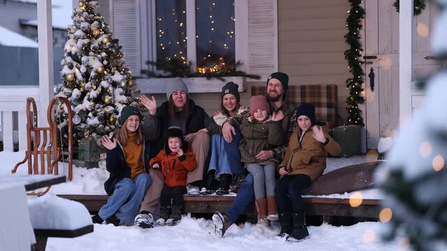 A large family in winter clothes and sweaters poses on the porch of a private country house on Christmas Day against the backdrop of the Christmas tree. The concept of holiday and togetherness.