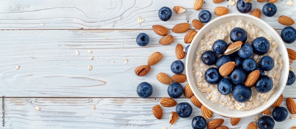 Poster top view of a white wooden background with a breakfast oatmeal featuring blueberries and almonds pro
