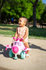 1 year old Latina baby girl playing outdoors on a toy plane