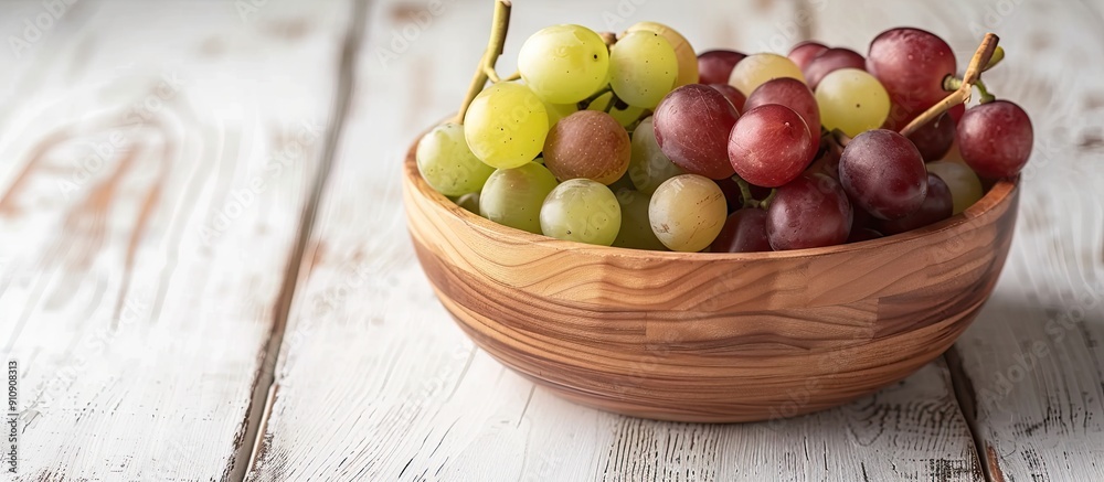 Poster wooden bowl filled with white and red grapes on a white wood table background with space for copying