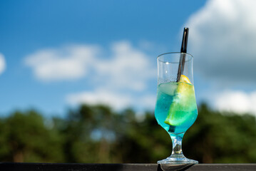 blue cocktail with ice and blue sky. glass of fresh cold blue lemonade with ice and straw