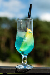blue cocktail with ice and blue sky. glass of fresh cold blue lemonade with ice and straw