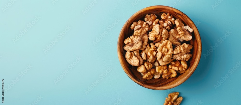 Poster walnut kernel halves arranged attractively in a wooden bowl captured from above on a colored backgro