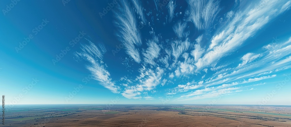 Poster a scenic aerial view featuring a clear blue sky adorned with wispy white clouds set against a vast e