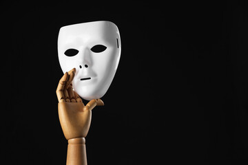 Wooden mannequin hand holding plastic mask on black background, space for text. Theatrical...