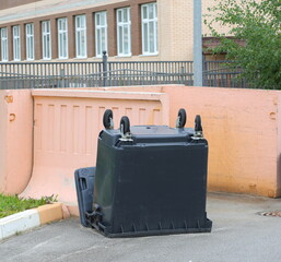 There is an inverted black plastic container by the pink wall of the waste place