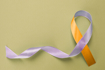 World Psoriasis Day. Orange and orchid awareness ribbon as symbol of support on olive color background, top view. Space for text