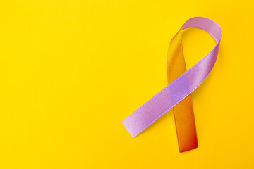 World Psoriasis Day. Orange and orchid awareness ribbon as symbol of support on yellow background, top view. Space for text