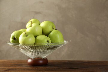 Glass vase with fresh green apples on wooden table against gray background, space for text