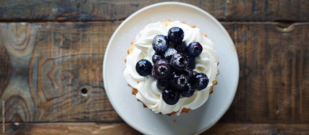 Poster vanilla sponge cake adorned with dairy whipped cream and blueberry sauce placed on a wooden table wi