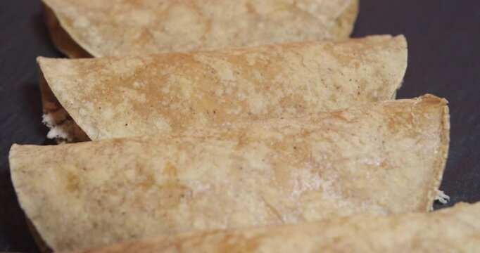Beautiful slow motion shot panning up close of a set of tacos or Mexican tortillas from the plate of chicken enchiladas in green sauce in a restaurant kitchen on a black plate.