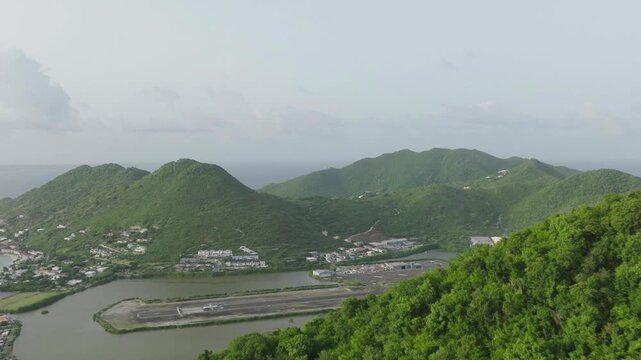 Aerial moving shot of Grand Case Airport with plane departing in Saint Martin with beautiful Caribbean landscape at background.