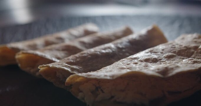 Beautiful close-up and slow motion shot of a group of 4 chicken enchiladas placed on a black plate and backlit in an industrial kitchen in a restaurant.
