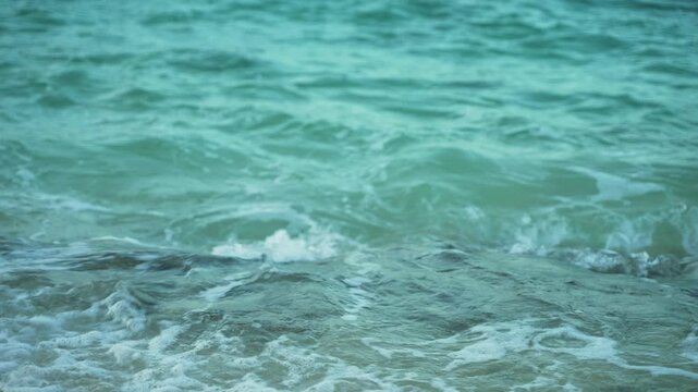 Closeup shot of turquoise sea water surf coming towards beach.