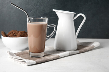 Glass of sweet chocolate milk and bowl with tasty cookies on white table