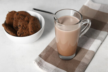 Glass of sweet chocolate milk and bowl with tasty cookies on white background