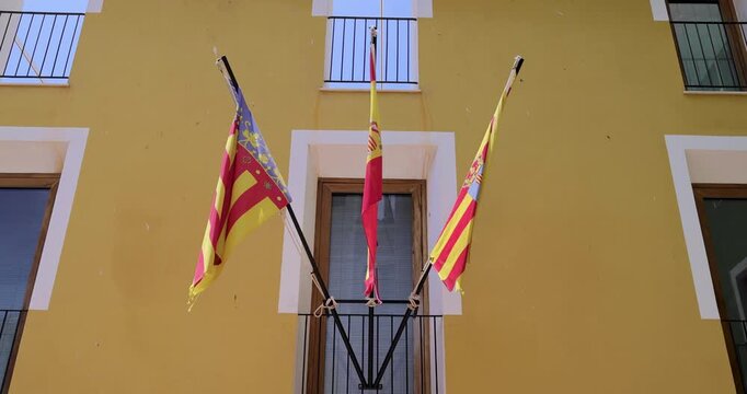 Slow motion footage of a selection of 3 spanish flags on a yellow building in the town of Villajoyosa in Alicante Spain showing the Spanish and Valencian Community flag on on a sunny day