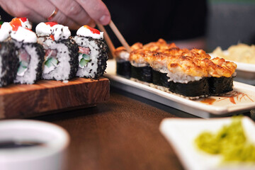 Composition of different kinds of sushi rolls placed on wooden board. Fresh Set of delicious Japanese Shushi. Eating sushi with chopsticks close up, food takeout. Variety of types sushi with caviar