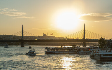 High resolution panoramic photograph capturing Istanbul's historic peninsula bathed in a crimson sunset glow. The city's iconic skyline silhouettes against the vibrant evening sky