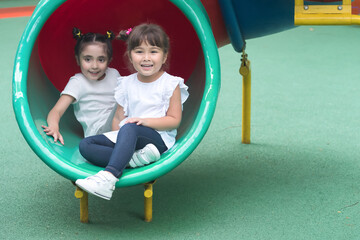 Happy smiling cute little girls, two preschooler female kids playing, sliding in kid playground...