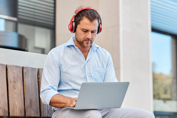 Business concept, man with headphones and laptop holding video conference on the street