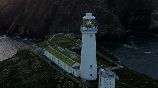 South Stack lighthouse aerial view circling island nautical beacon below mountain shore at dusk