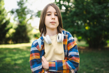 Confident boy with wireless headphones and arms crossed at park