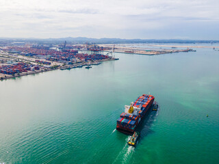 the aerial perspective of a cargo ship being loaded and unloaded at a bustling seaport and sailing out of the mainland