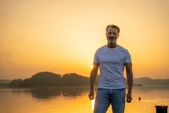 Smiling man standing near lake at sunrise - Powered by Adobe