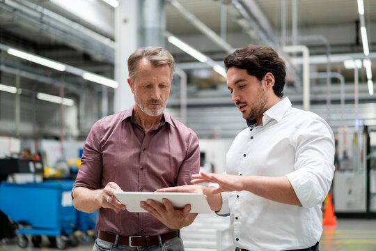 Business colleagues discussing strategies over tablet PC standing in factory