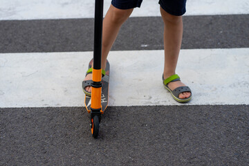 A child on a scooter walks along a pedestrian crossing