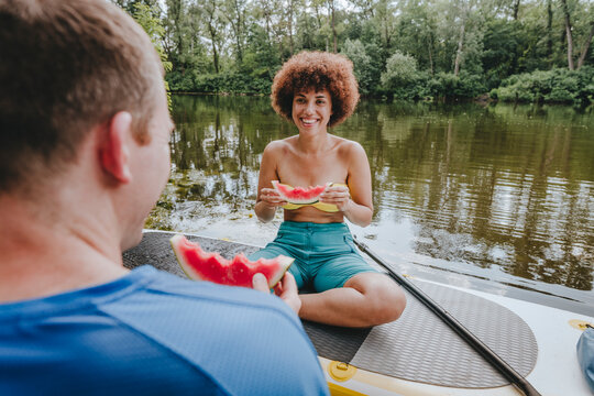 Smiling friends having watermelon on paddleboard in lake