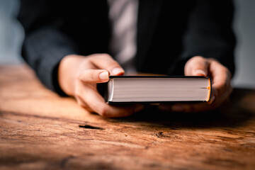 Hands folded in prayer on a Holy Bible in church concept for faith, spirituality and religion,...