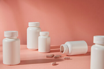 Pink background photo from frontal shot, plenty unbranded medicine bottle in white evenly arranged on the table top, one flat lay with some falling out capsules. Designing and advertising space