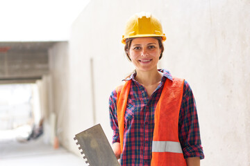 Portrait of confident young female construction worker wearing workwear holding trowel at site