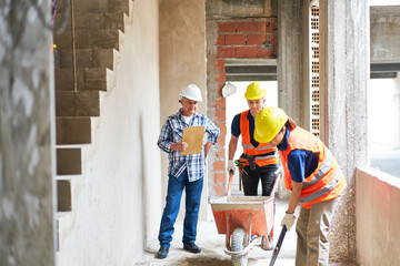 Senior male contractor supervising masons mixing mortar at corridor in incomplete house