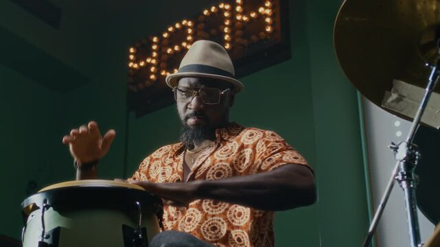 African American drummer playing conga, then stopping and looking at camera during rehearsal in bar
