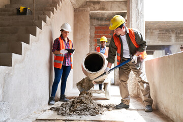 Young multiethnic male and female masons mixing cement by supervisor at incomplete housing...