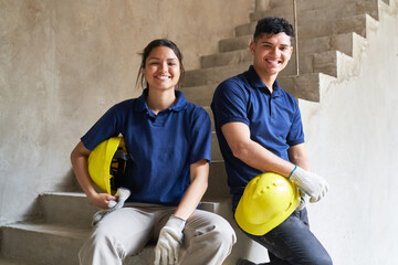 Portrait of smiling young male and female coworkers sitting on incomplete staircase in corridor at...