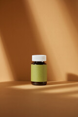 Frontal shot mock up photography with a blank green label medicine jar, isolated against on brown background. Blank space for advertising and designing